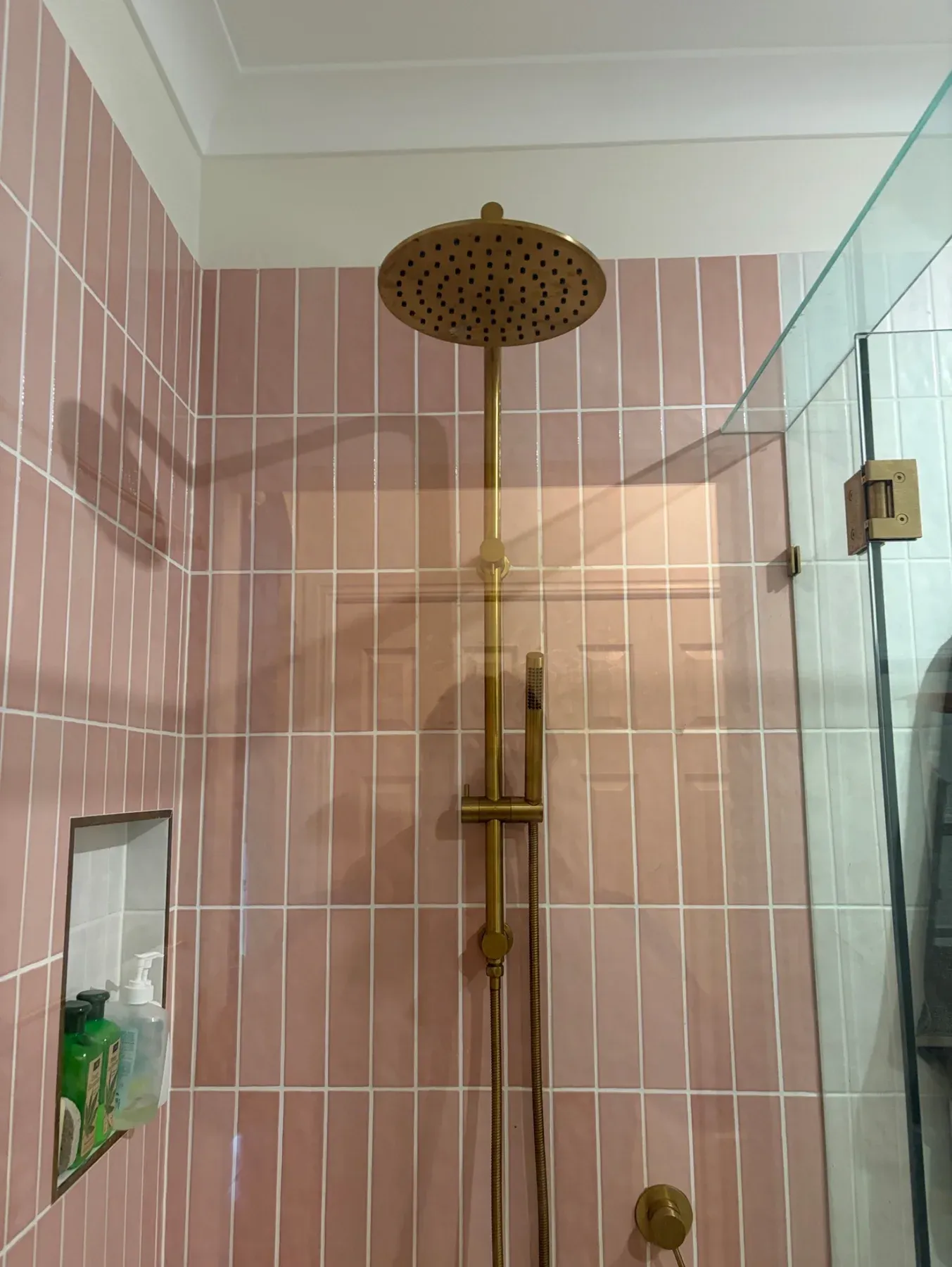 Brass shower fittings with pink tiles and a glass screen