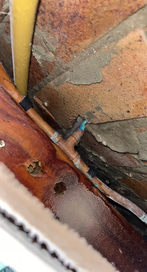 Water leaking from copper pipework exposed in a brick wall cavity