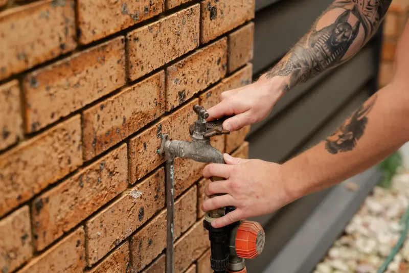 Hands using a wrench to maintain a garden tap on a brick wall
